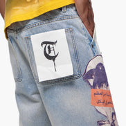 Close-up of a person wearing a yellow shirt and light blue jeans with patches, on a white background.