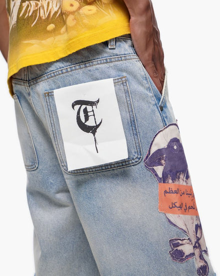 Close-up of a person wearing a yellow shirt and light blue jeans with patches, on a white background.