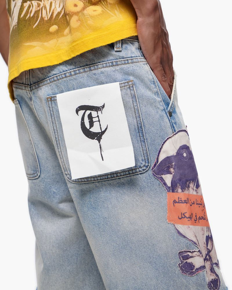Close-up of a person wearing a yellow shirt and light blue jeans with patches, on a white background.