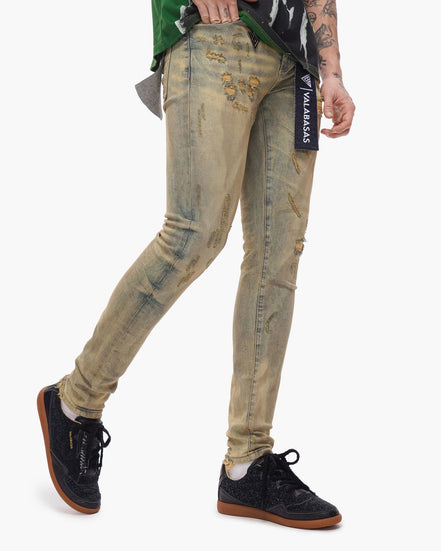Person wearing distressed beige jeans with a brand label on a white background