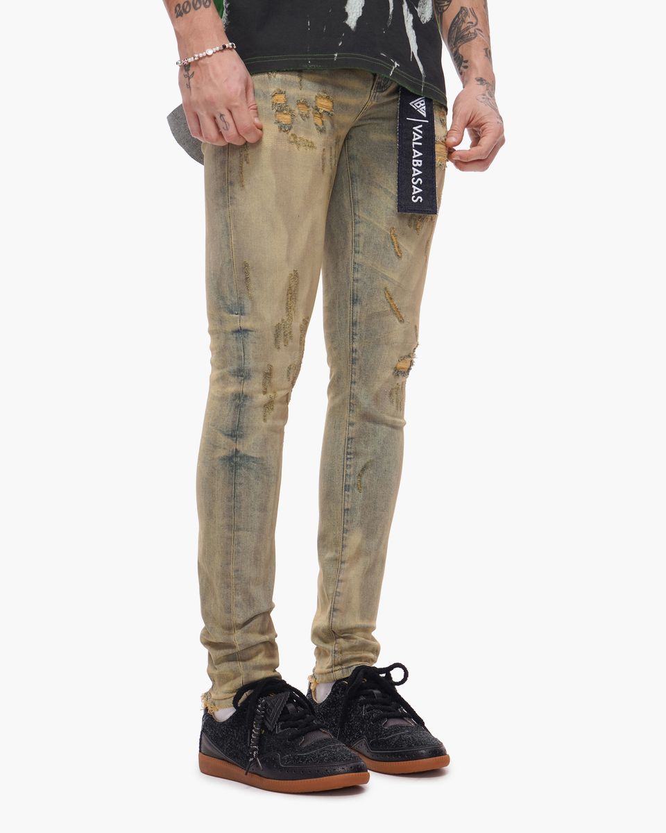 Person wearing distressed beige jeans with a brand label on a white background