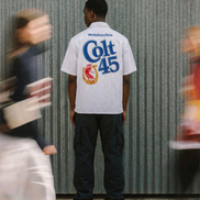 Person wearing a white shirt with 'Colt 45' branding in front of a corrugated metal wall.