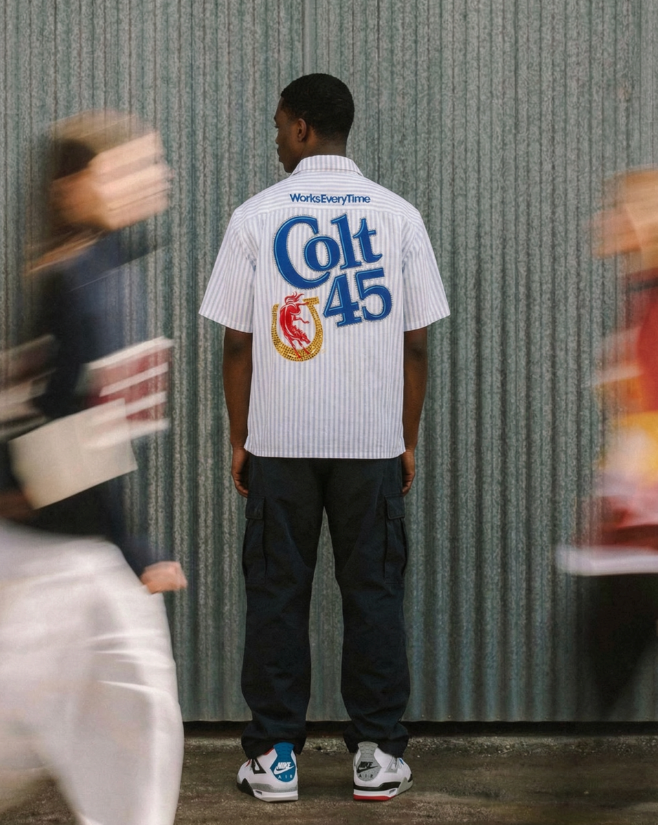 Person wearing a white shirt with 'Colt 45' branding in front of a corrugated metal wall.
