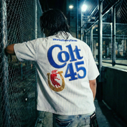 Person wearing a 'Colt 45' shirt leaning against a chain-link fence at night.