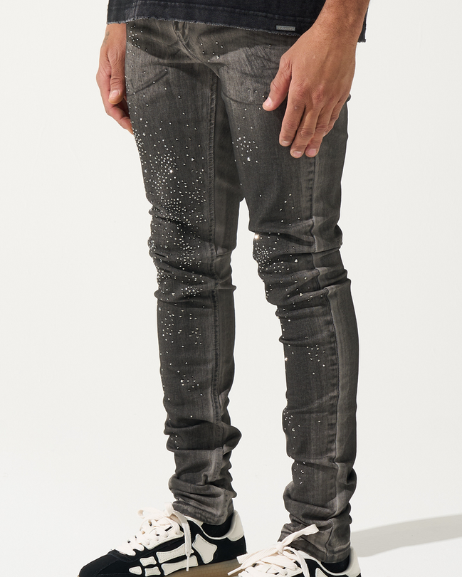 Person wearing black jeans with white speckles and black and white sneakers on a white background