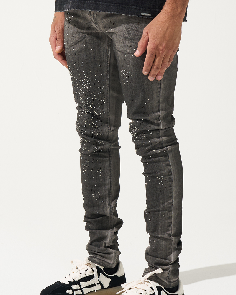Person wearing black jeans with white speckles and black and white sneakers on a white background