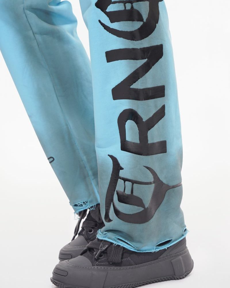 Light blue pants with black text and graphics worn with black sneakers on a light gray background