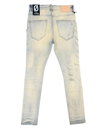 Back view of light-wash distressed jeans with faded yellowing and scuff marks, featuring a black brand patch on the left back pocket.