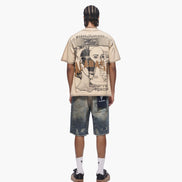 Person wearing a beige t-shirt with graphic design and distressed blue shorts on a white background