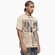Man wearing a beige t-shirt with graphic design and text, standing against a white background