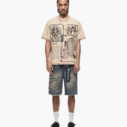 Man wearing a beige graphic t-shirt and distressed denim shorts on a white background
