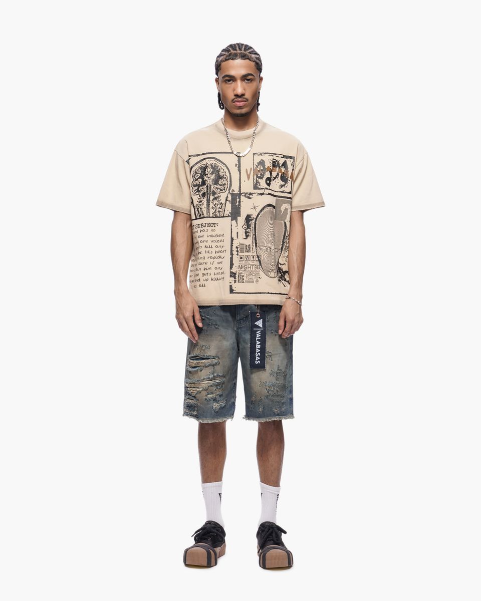 Man wearing a beige graphic t-shirt and distressed denim shorts on a white background