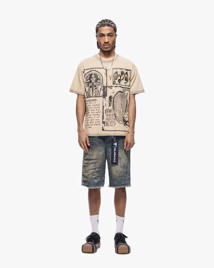 Man wearing a beige graphic t-shirt and distressed denim shorts on a white background