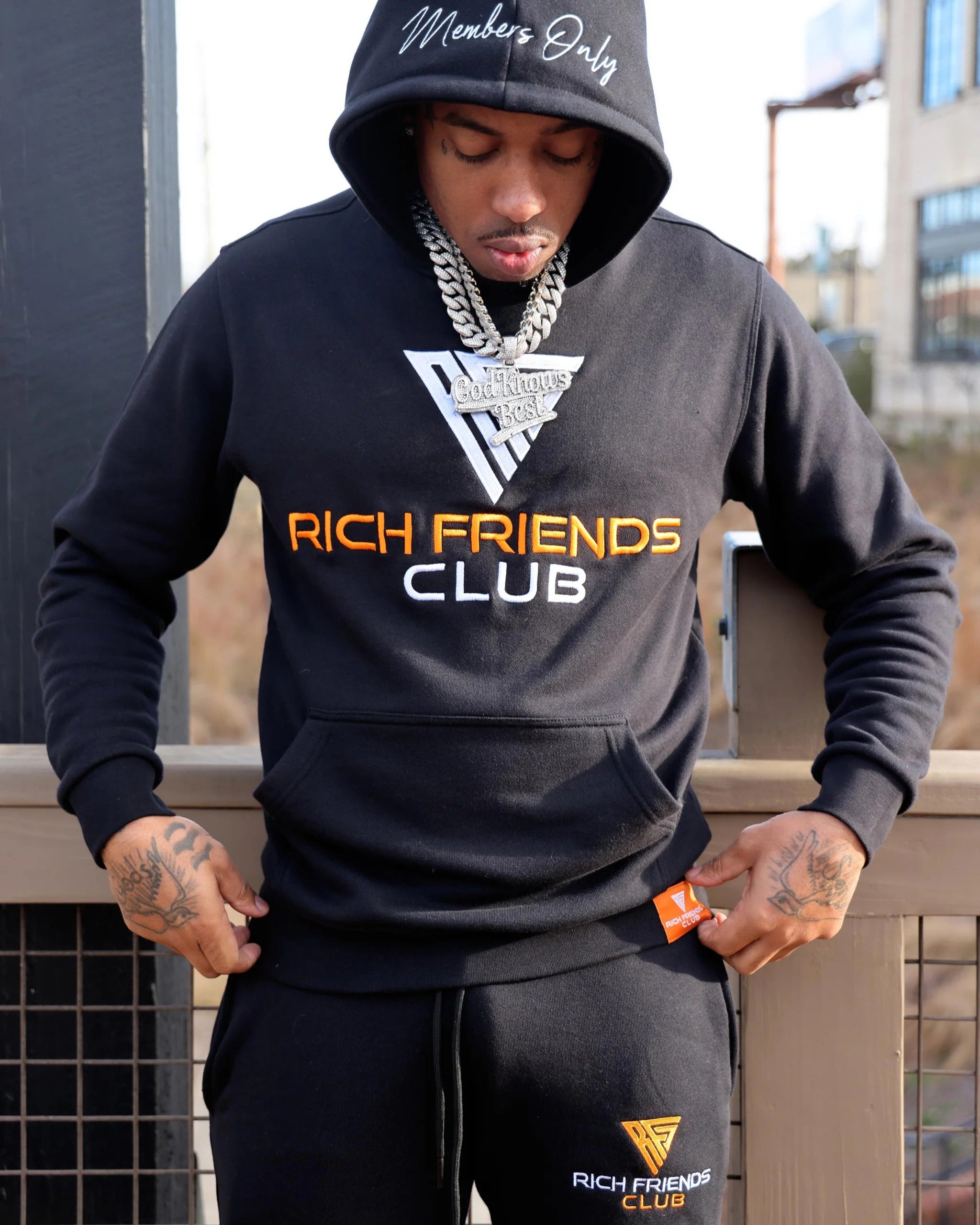 Person wearing a 'Rich Friends Club' hoodie and pants with text on a blurred background