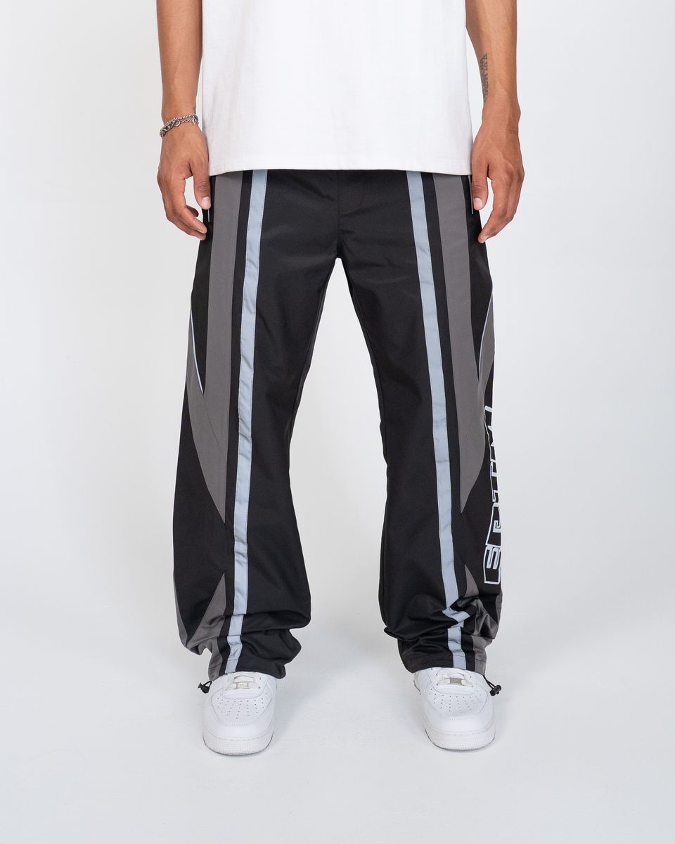 Black track pants with gray stripes worn by a person on a white background