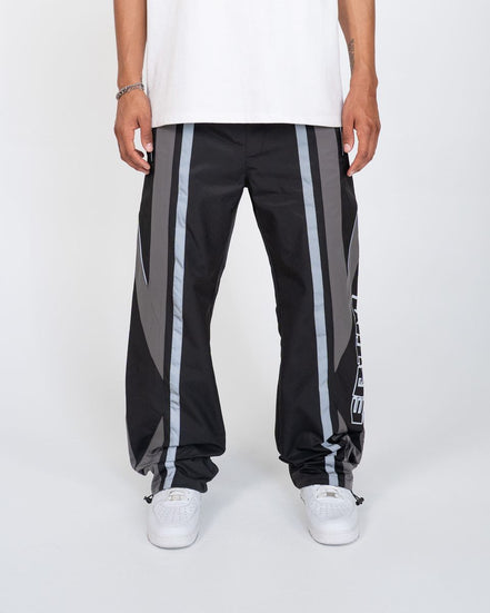 Black track pants with gray stripes worn by a person on a white background