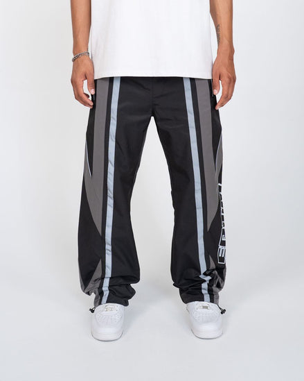 Black track pants with gray stripes worn by a person on a white background