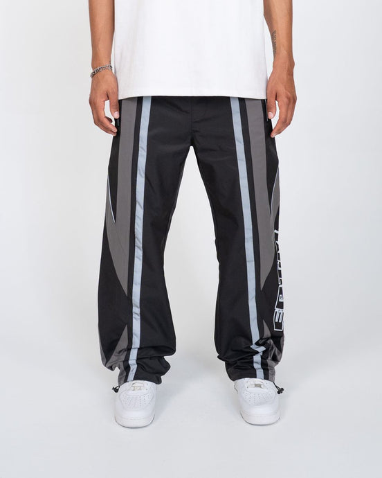 Black track pants with gray stripes worn by a person on a white background