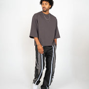 Man wearing a gray oversized t-shirt and black track pants with white stripes on a white background