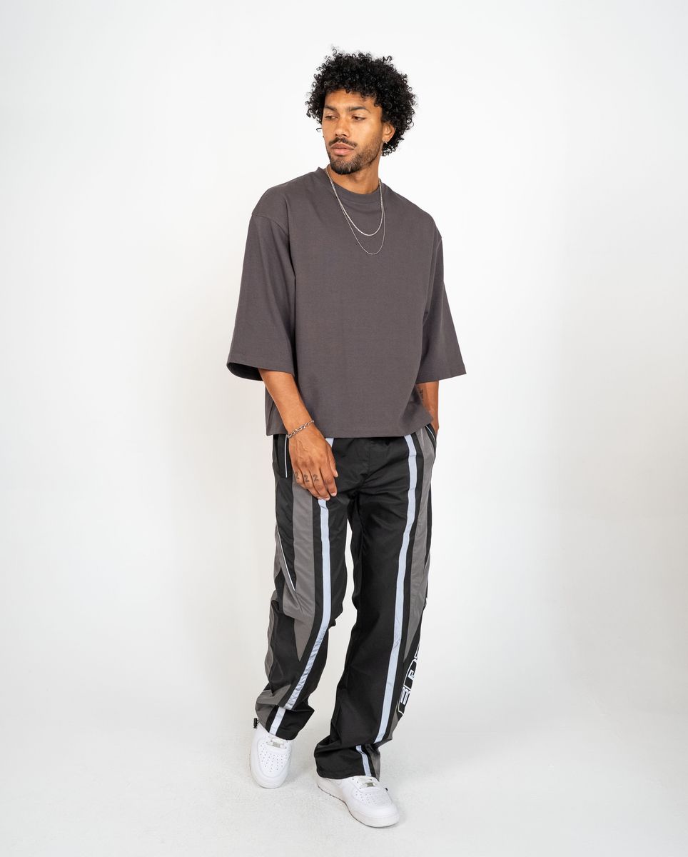 Man wearing a gray oversized t-shirt and black track pants with white stripes on a white background