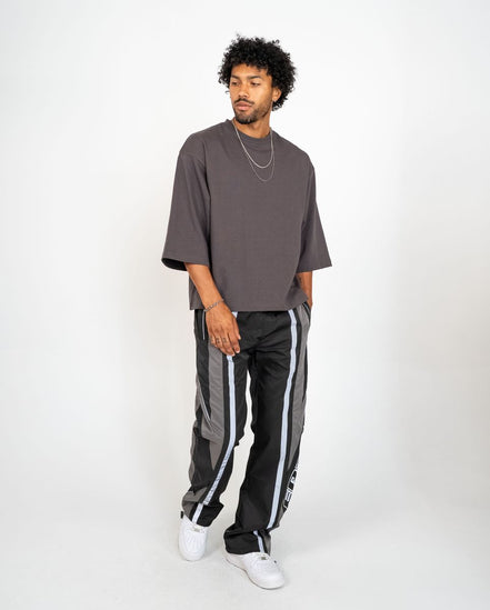 Man wearing a gray oversized t-shirt and black track pants with white stripes on a white background