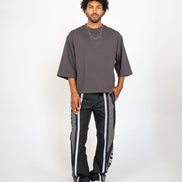 Man wearing a gray oversized t-shirt and black pants with white stripes on a white background
