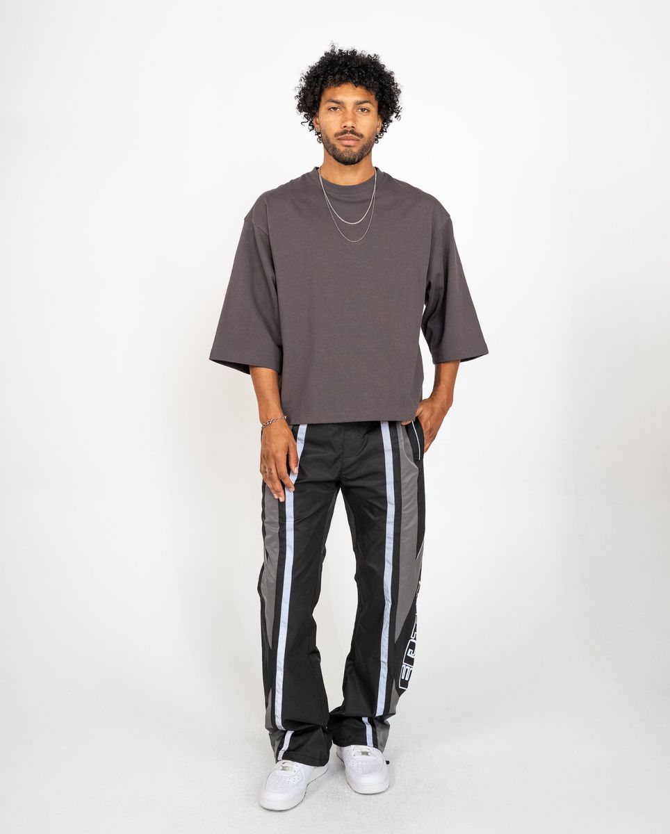 Man wearing a gray oversized t-shirt and black pants with white stripes on a white background