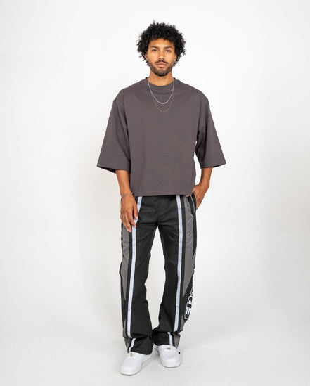 Man wearing a gray oversized t-shirt and black pants with white stripes on a white background