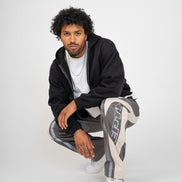 Man wearing a black hoodie and gray pants with white text, sitting on a white background