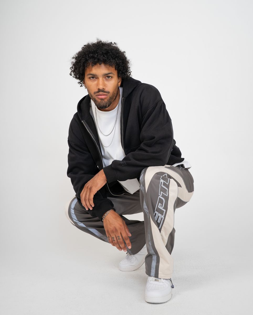 Man wearing a black hoodie and gray pants with white text, sitting on a white background