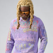 Man wearing a colorful graphic sweatshirt with sunglasses and braided hair on a plain background