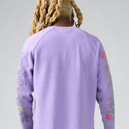 Person wearing a purple sweatshirt with colorful designs on sleeves against a gray background