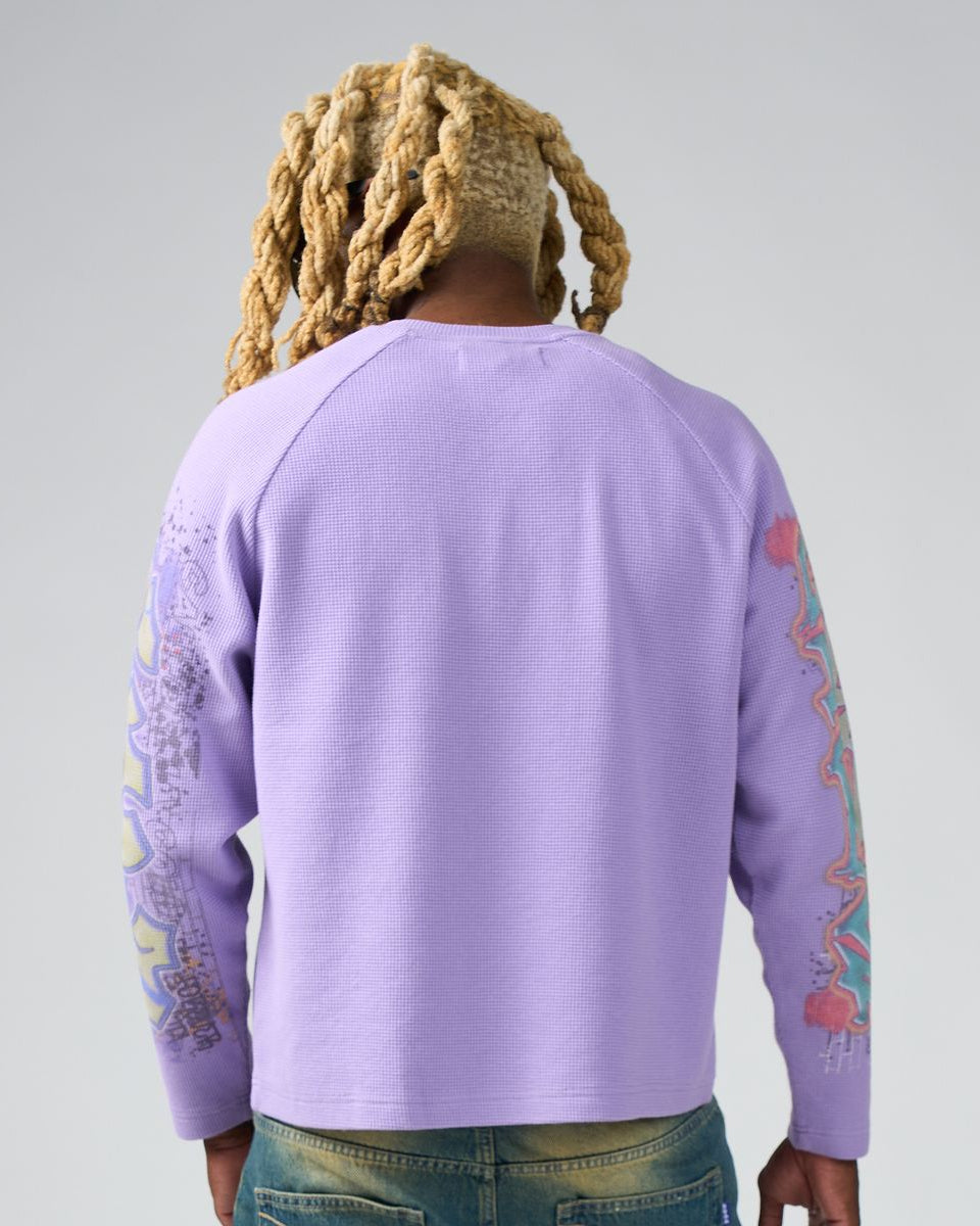 Person wearing a purple sweatshirt with colorful designs on sleeves against a gray background
