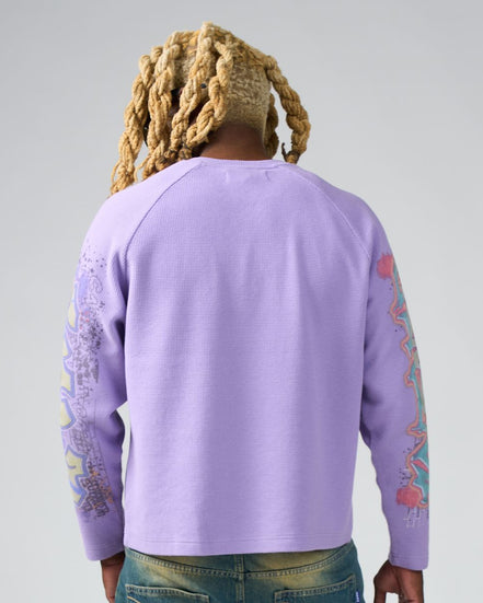 Person wearing a purple sweatshirt with colorful designs on sleeves against a gray background