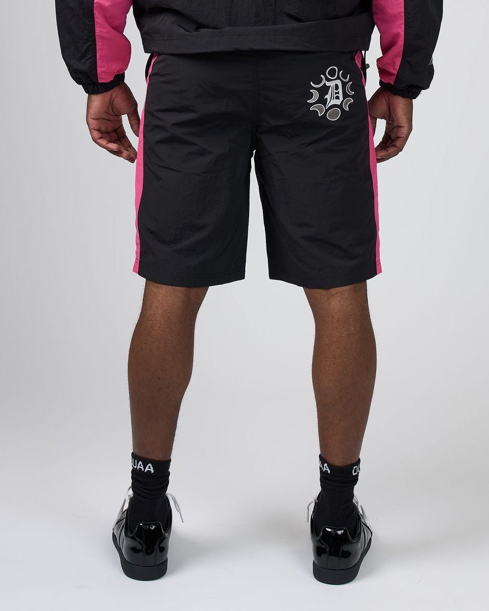 Black athletic shorts with pink side panels and a white graphic logo on the left hip, shown on a model from the back against a light gray studio background.