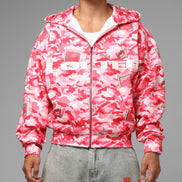 Person wearing a pink camouflage jacket with brand logos on a gray background