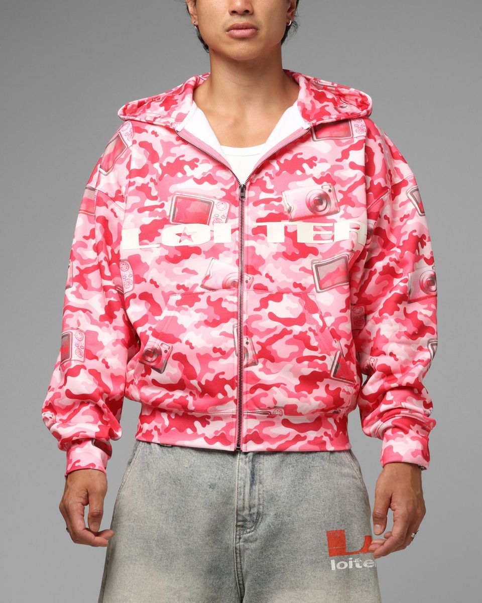 Person wearing a pink camouflage jacket with brand logos on a gray background