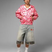 Person wearing a pink camouflage jacket and light blue jeans on a gray background