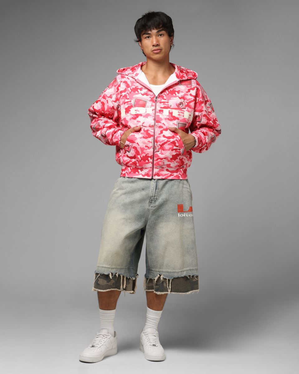 Person wearing a pink camouflage jacket and light blue jeans on a gray background