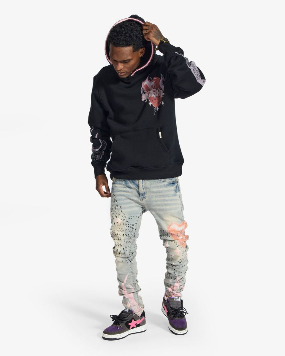 Person wearing a black hoodie with a graphic design and light blue distressed jeans on a white background