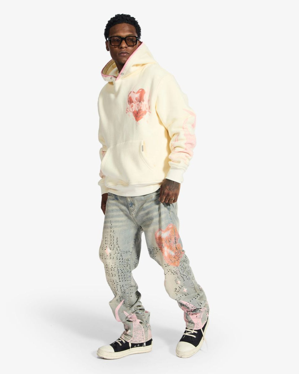 Person wearing a light-colored hoodie with heart designs and patterned pants on a white background