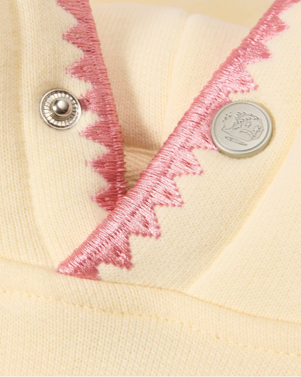 Close-up of a cream-colored garment with pink embroidery and two buttons.