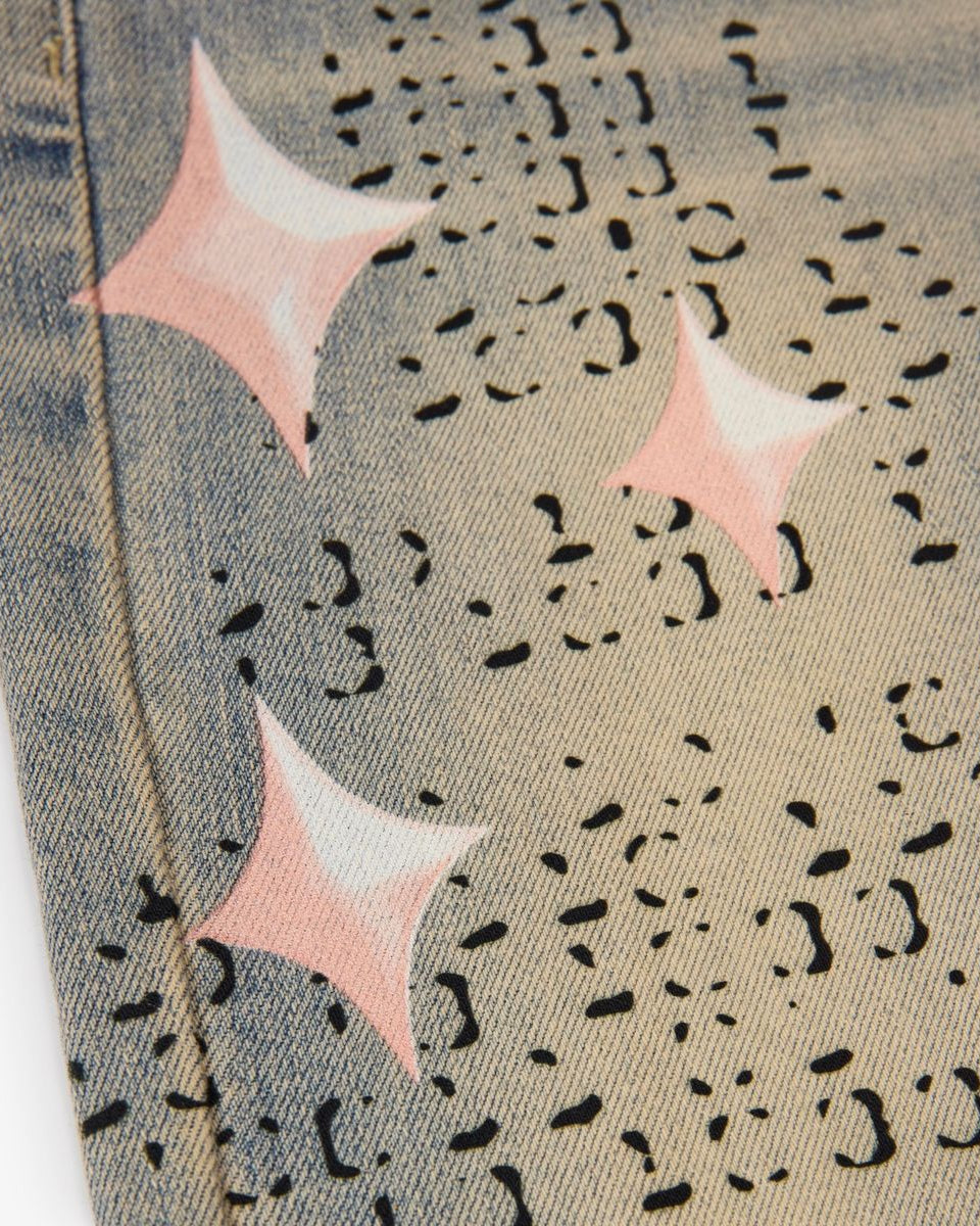 Close-up of a denim fabric with pink star patterns and black abstract shapes.