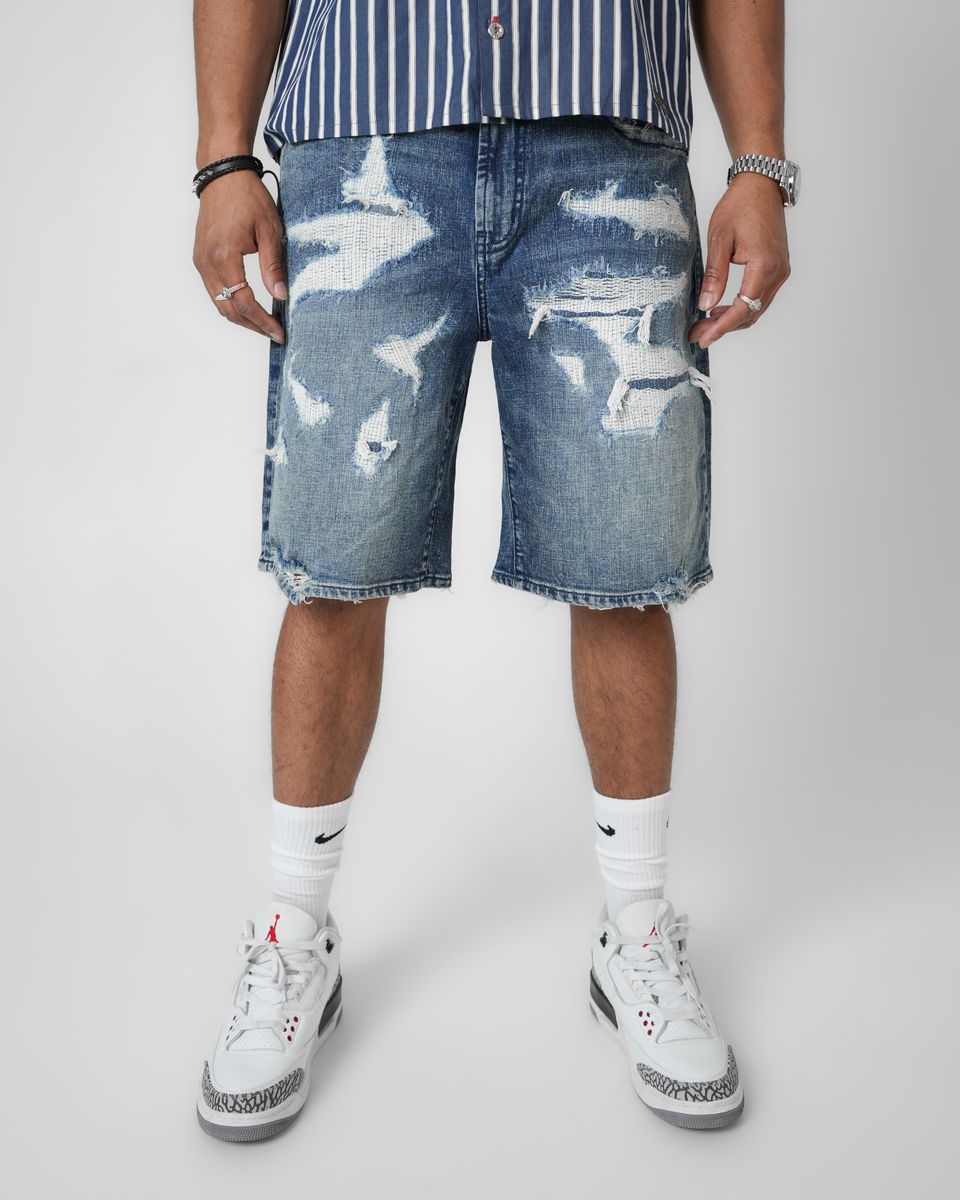 Person wearing distressed denim shorts with a plain background