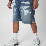 Person wearing distressed blue denim shorts with white sneakers on a plain background