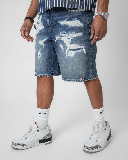 Person wearing distressed blue denim shorts with white sneakers on a plain background