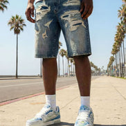 Person wearing distressed denim shorts and white sneakers on a sunny day with palm trees in the background.