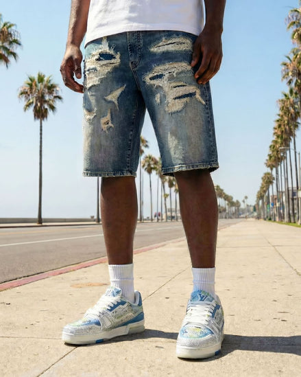 Person wearing distressed denim shorts and white sneakers on a sunny day with palm trees in the background.