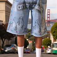 Person wearing denim shorts with 'CITY OF DENIM' text and penguin design, standing on a street with a cityscape background.
