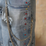 Close-up of blue jeans with decorative chains and beads.